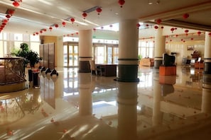 Um hall amplo com piso lustroso, pilares imponentes e decorações vermelhas penduradas.