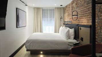 A modern hotel room with a large bed, a brick accent wall, a flat-screen TV, and a window with curtains.