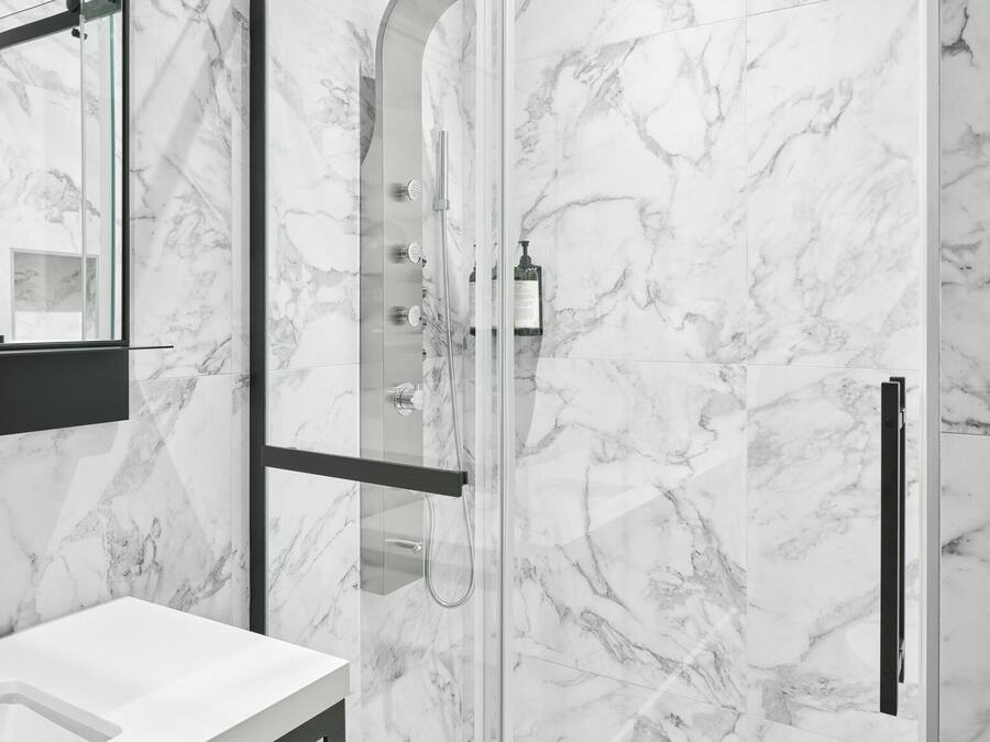 Une salle de bain moderne avec une douche à parois de verre, des murs en marbre et un lavabo blanc.