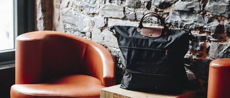 A modern interior with a brick wall, leather armchairs, a wooden coffee table, and a black handbag.