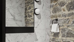 A modern bathroom with a marble vanity, a large mirror, a stone wall, and a towel rack. - Le Petit Hôtel Vieux-Montréal | Notre-Dame (Montreal)