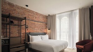 A modern hotel room with a brick wall, a bed with white linens, a red chair, and a wooden floor. - Le Petit Hôtel Vieux-Montréal | Notre-Dame (Montreal)