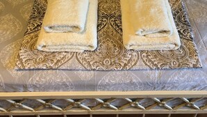 Ein ordentlich bezogenes Bett mit einem gemusterten Bettbezug, zwei Kissen und zwei gefaltete Handtücher auf einem dekorativen Tablett.