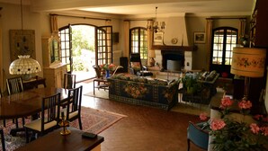 Ein traditionelles Wohnzimmer mit Kamin, einem Essbereich mit Holztisch und -stühlen sowie einer Sofagarnitur.