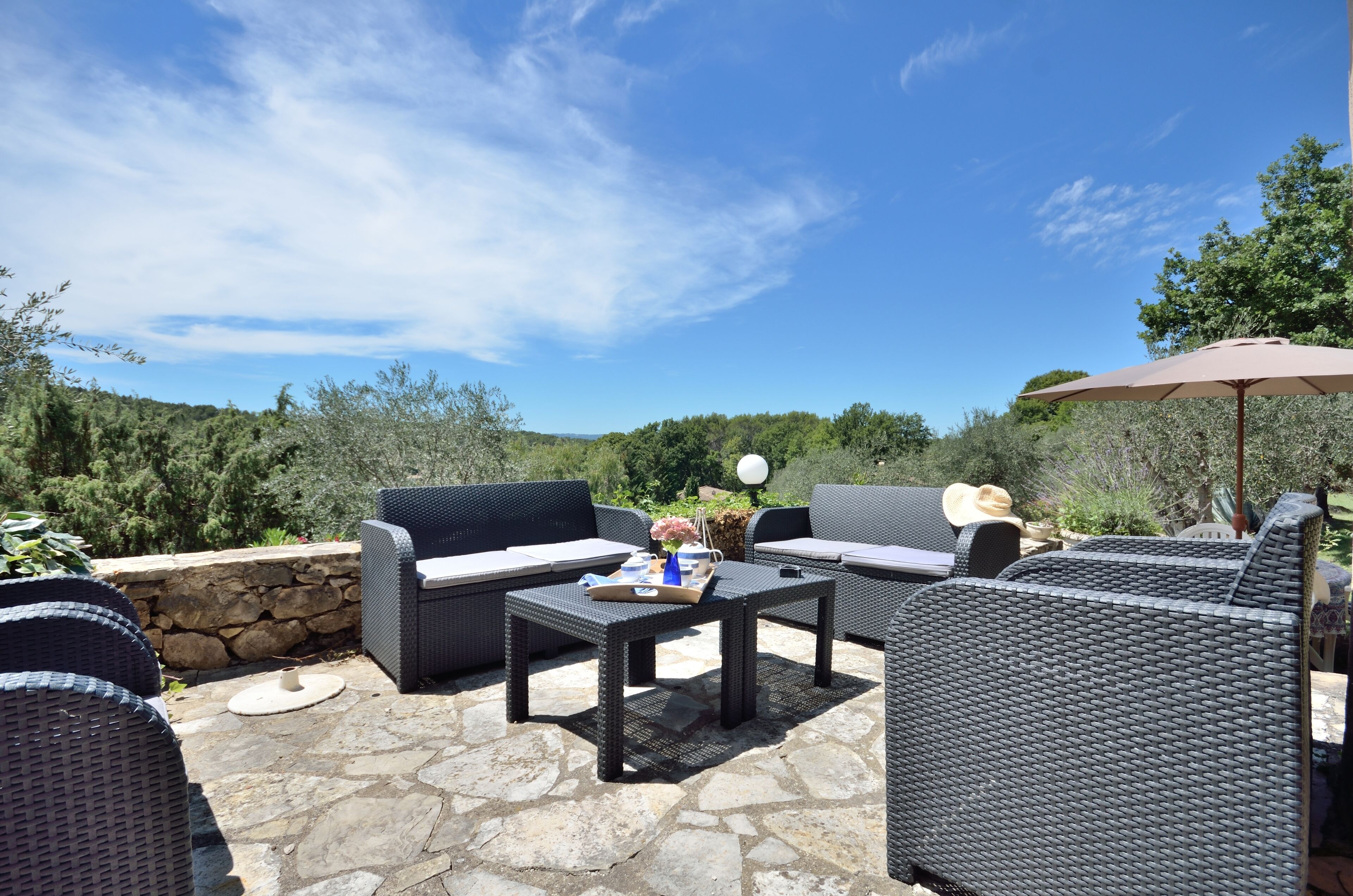 An outdoor patio with wicker furniture, stone flooring, and a view of the surrounding landscape.