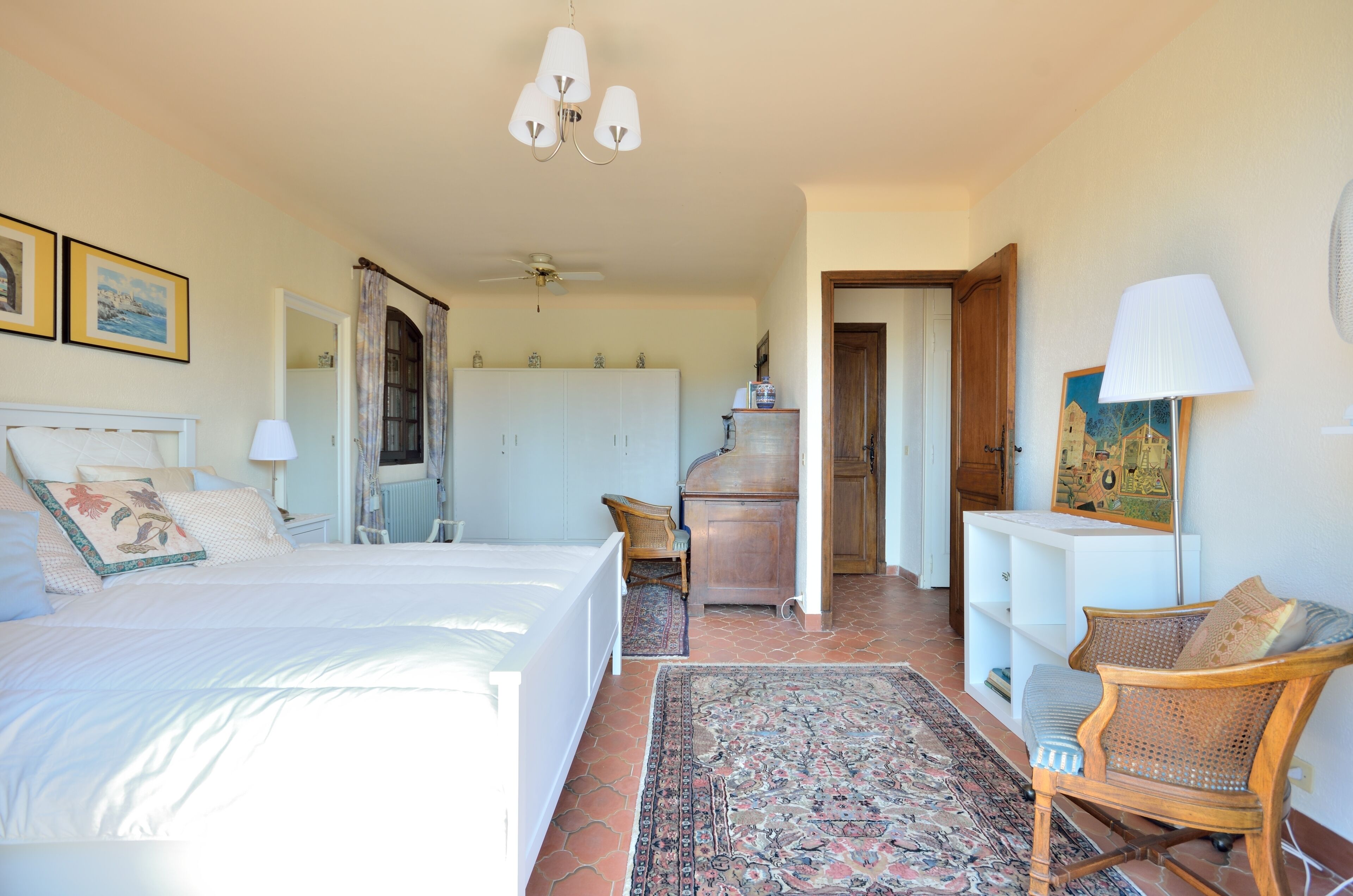 A bedroom with a large bed, a chair, a small table, and a wardrobe.