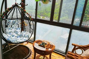 A room with a large window, a hanging chair, a round table, and a small round rug.
