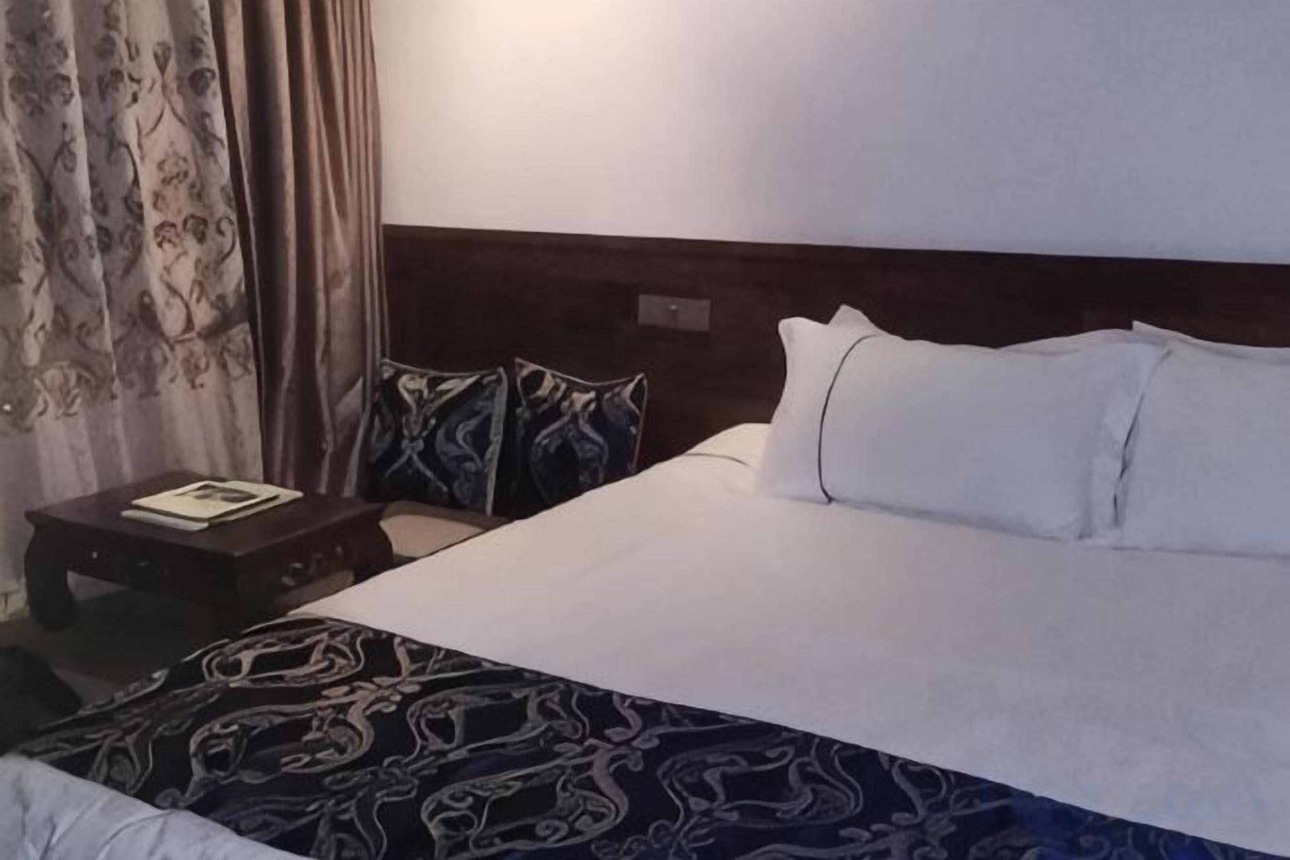 Ein Hotelzimmer mit einem großen Bett, einem Nachttisch mit einem Buch und einer gemusterten Tagesdecke.