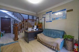 Zona de recepción con escalera, mostrador de recepción, sofá azul y un tablón de anuncios.