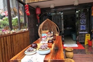Una mesa de madera con vajilla, un farol rojo colgante y una silla de mimbre al fondo.