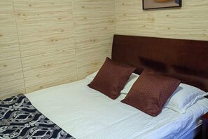 A neatly made bed with a patterned bedspread and two brown pillows, set against a wooden wall with a framed picture above it. - Yandang Mountain Mingxiu Pavilion Inn (Yueqing)