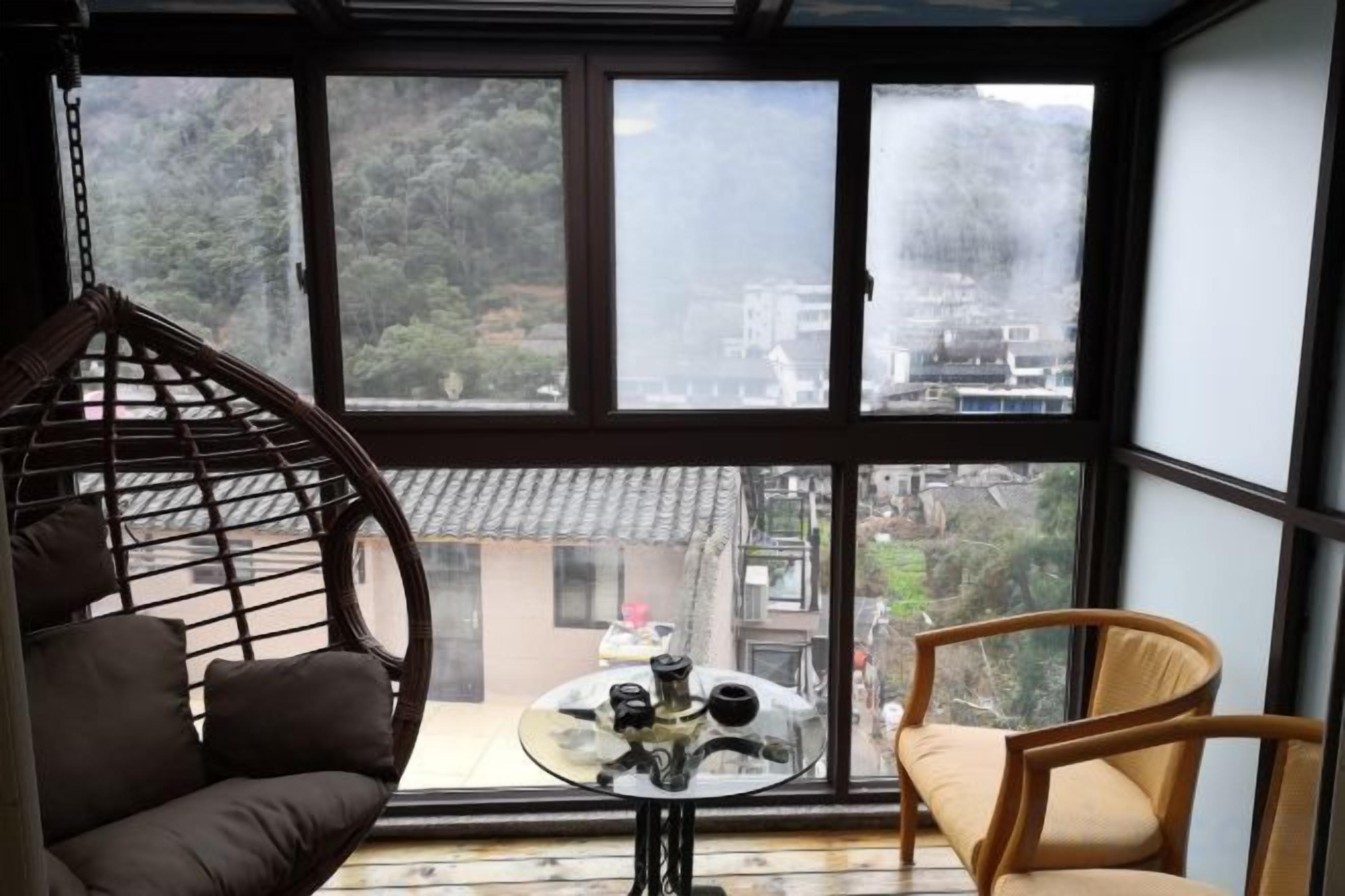 A room with a large window, a hanging chair, a sofa, and a small table with a teapot.