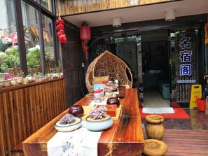 A traditional Chinese restaurant entrance with a wooden table set for dining, a woven chair, and a sign with Chinese characters. - Yandang Mountain Mingxiu Pavilion Inn (Yueqing)