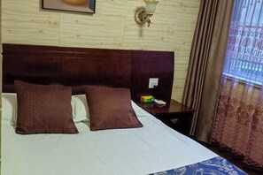 A hotel room with a wooden headboard, two brown pillows, a white bedspread, a nightstand with a lamp, and a window with curtains. - Yandang Mountain Mingxiu Pavilion Inn (Yueqing)