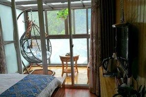 Una habitación con cama, sillón colgante, mesita y vistas al exterior.