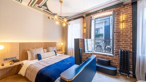 Quarto de hotel moderno com uma cama grande, uma escrivaninha com televisão de tela plana, uma janela com vista exterior e uma parede de tijolos.