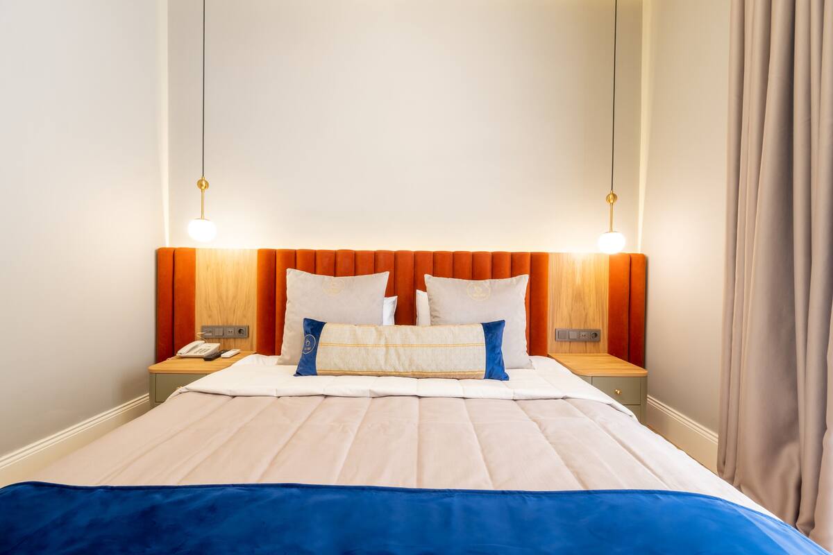 A neatly made bed with a blue bedspread, two bedside tables with lamps, and a wooden headboard.