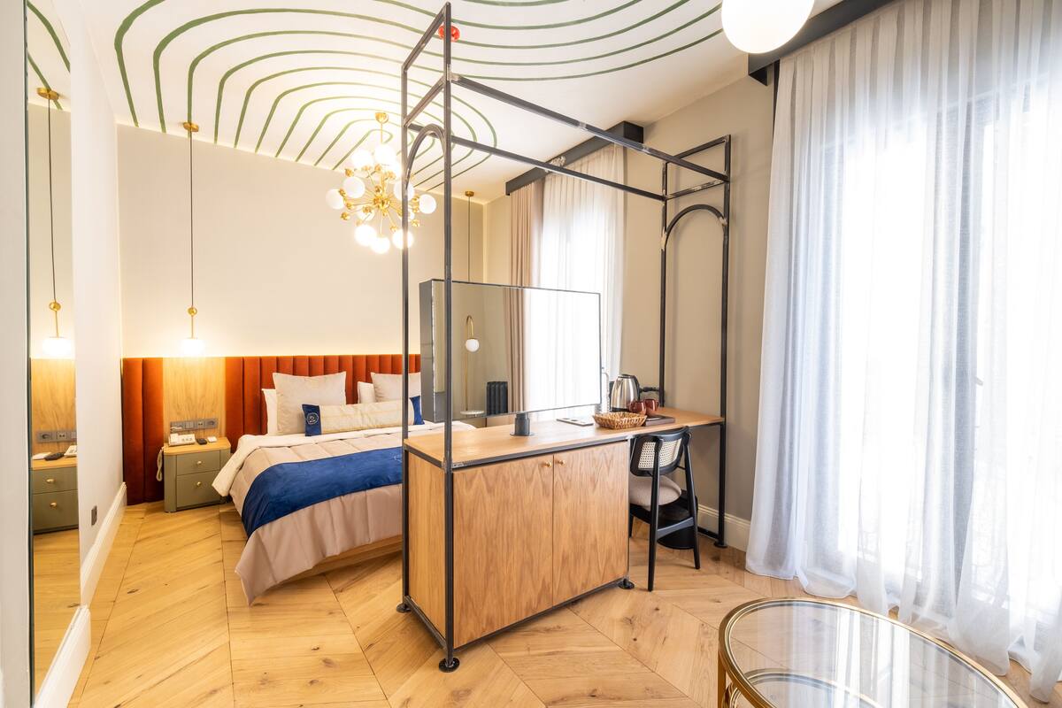 A modern hotel room with a bed, desk, chair, and a large mirror.