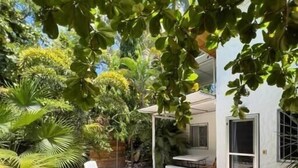 Un espacio de estar al aire libre cubierto con sillas blancas y una mesa, rodeado de abundante follaje y suelo de grava.