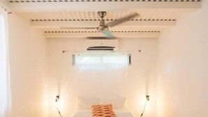 Un dormitorio con cama, ventilador de techo, aire acondicionado y lámparas de noche.