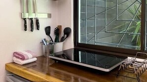 Una cocina con estantes de madera que sostienen utensilios, una ventana con un diseño geométrico y una encimera con un hervidor y una bandeja.