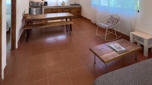 A spacious kitchen with a wooden ceiling, a dining area with a bench, and a seating area with a chair and table. - Guiones 1BR: Walk to Beach and Work (Playa Guiones)