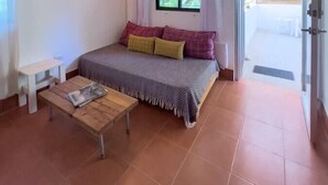 A bedroom with a bed, a small table, a hanging light fixture, and a window with curtains. - Guiones 1BR: Walk to Beach and Work (Playa Guiones)