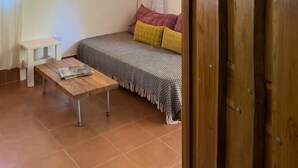 A cozy room with a wooden ceiling, a bed with patterned bedding, a small table with a magazine, and a hanging light fixture. - Guiones 1BR: Walk to Beach and Work (Playa Guiones)
