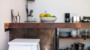 A kitchen counter with a bowl of fruit, a coffee maker, and a metal pot on the shelf.