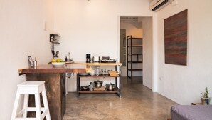 A compact kitchen with a wooden countertop, a white stool, and a metal shelf unit.