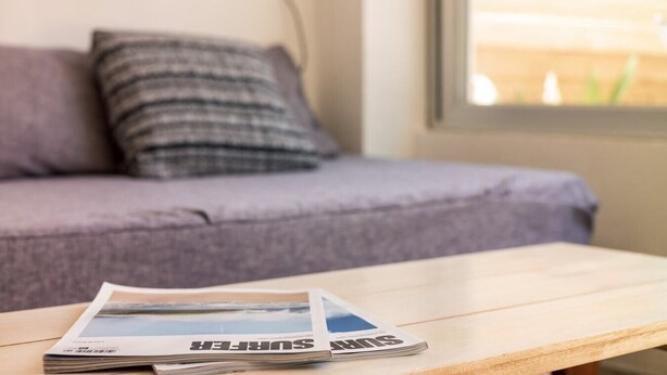 A magazine on a wooden table with a sofa and a window in the background.
