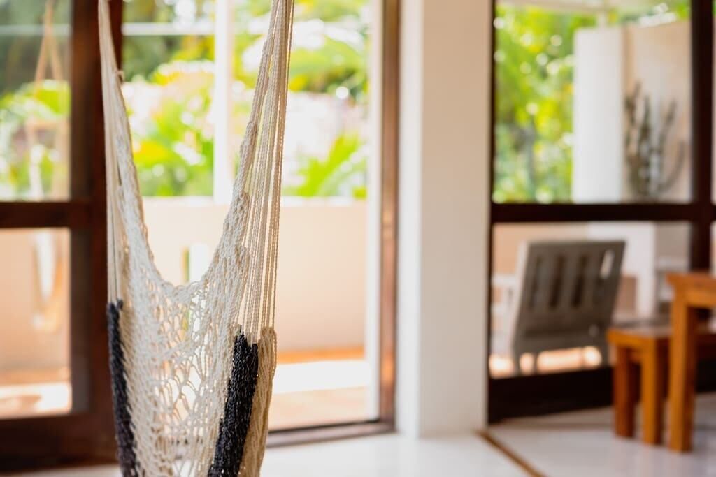 Un hamac est suspendu à l’intérieur, offrant une vue sur la verdure à l’extérieur, visible à travers de grandes fenêtres.