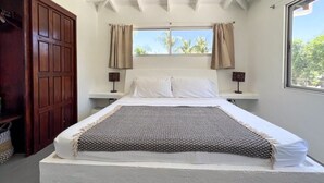 Een slaapkamer met een bed, een plafondventilator, een raam met gordijnen en een houten kledingkast.