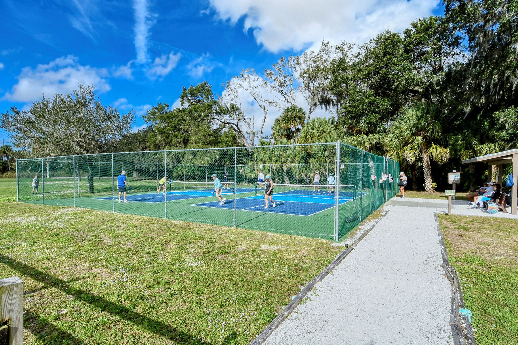 Una cancha de tenis al aire libre con una red, rodeada de una valla y árboles.