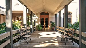 A covered wooden deck with benches, potted plants, and a building entrance in the background. - Homey 1bed/1bath condo The Meadows Pool View (Sarasota)