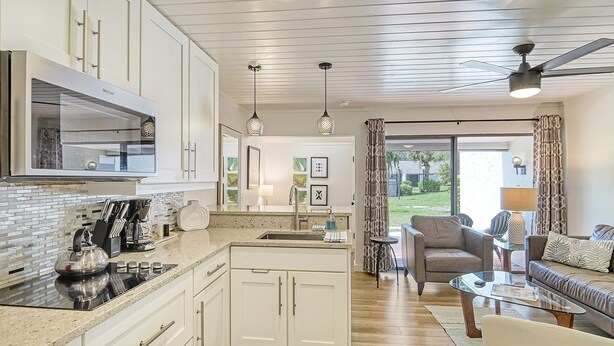 A modern kitchen with white cabinets, a stainless steel refrigerator, and a dining area with a glass table and leather sofa. - Homey 1bed/1bath condo The Meadows Pool View (Sarasota)