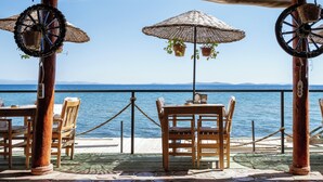 A seaside terrace with wooden tables and chairs, wicker parasols, and potted plants. - Ada Tiny House (Ayvacik)
