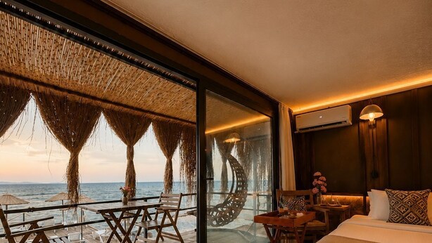 A modern hotel room with a large glass wall, a wooden deck with outdoor furniture, and a bed with a view of the ocean. - Ada Tiny House (Ayvacik)