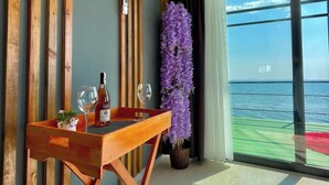 A room with a wooden table, a potted purple plant, and a view of the sea through large windows. - Ada Tiny House (Ayvacik)