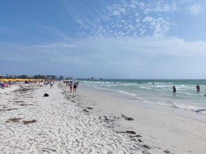 Una playa con gente caminando y nadando, y sombrillas dispuestas a lo largo de la orilla.
