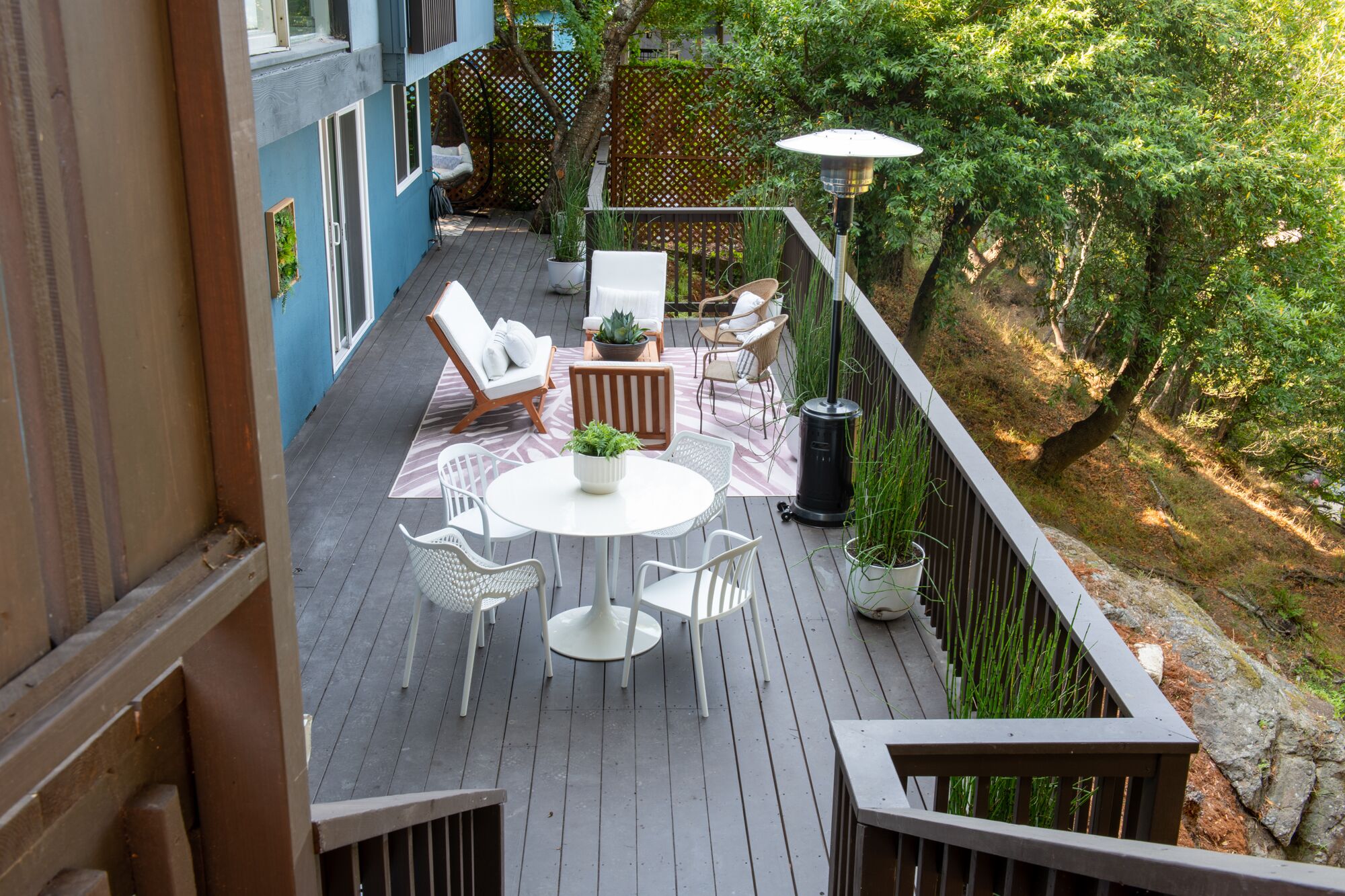 A deck with a round table and chairs, surrounded by potted plants and a hanging chair.