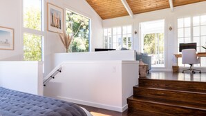 Une chambre spacieuse avec un grand lit, un escalier menant à un étage supérieur et une vue sur l’extérieur grâce à de grandes fenêtres.