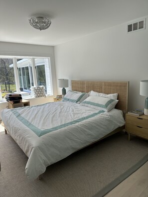 A bedroom with a large bed, two bedside tables, a window, and a ceiling light fixture. - Palm Springs Vibes on the North Fork (Southold)