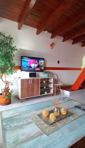 A living room with a TV on a wooden cabinet, a plant, and a decorative table with a vase and candle-like objects.