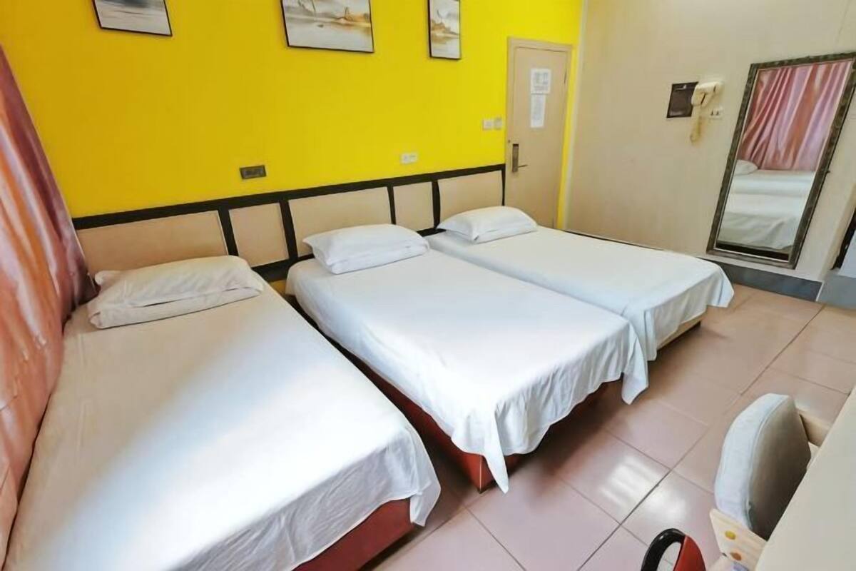A room with three single beds, a door, a mirror, and a small table with a chair.