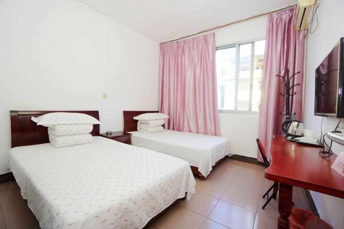 A hotel room with two beds, a desk with a chair, a TV, and a window with curtains.