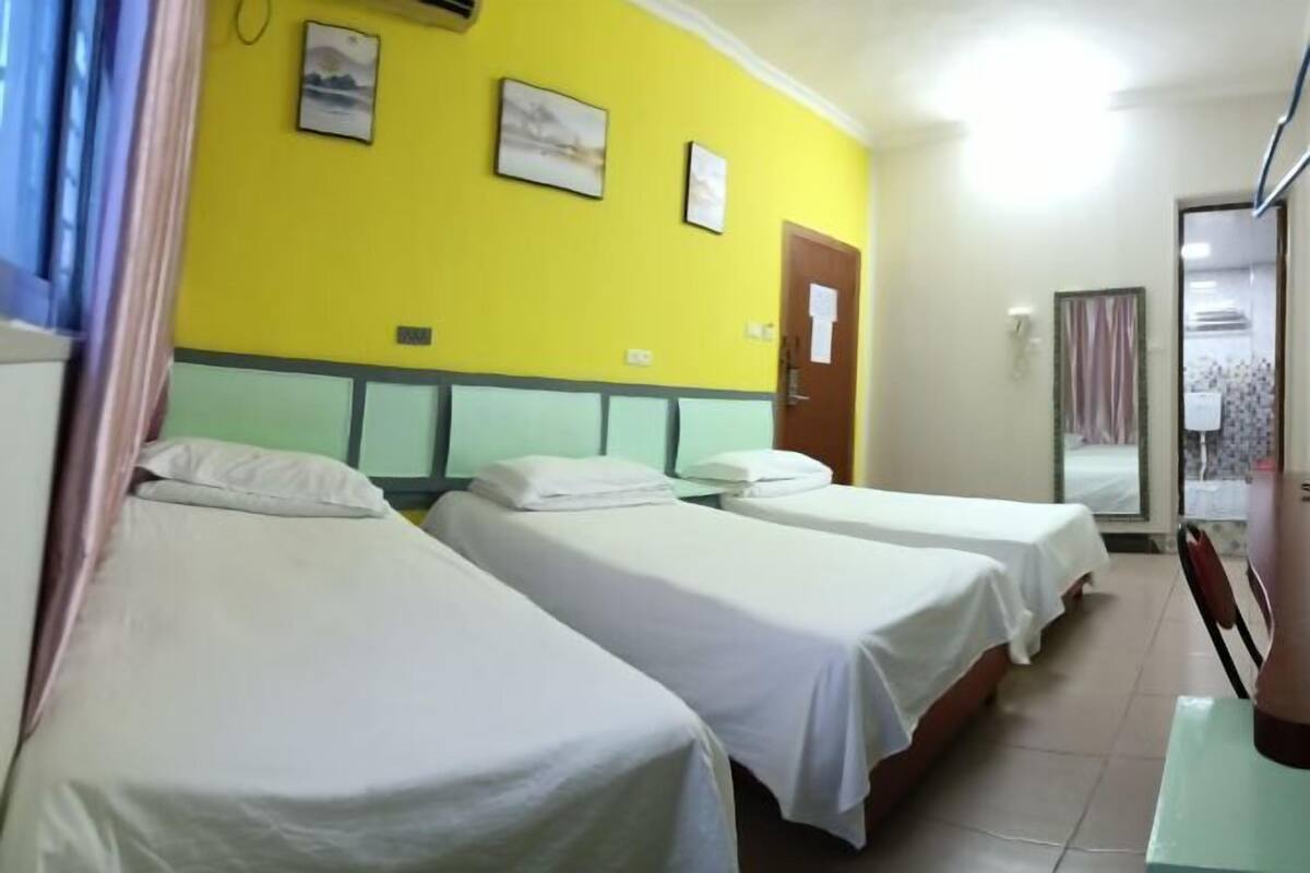 A hotel room with three single beds, a yellow wall, and a door with a sign.