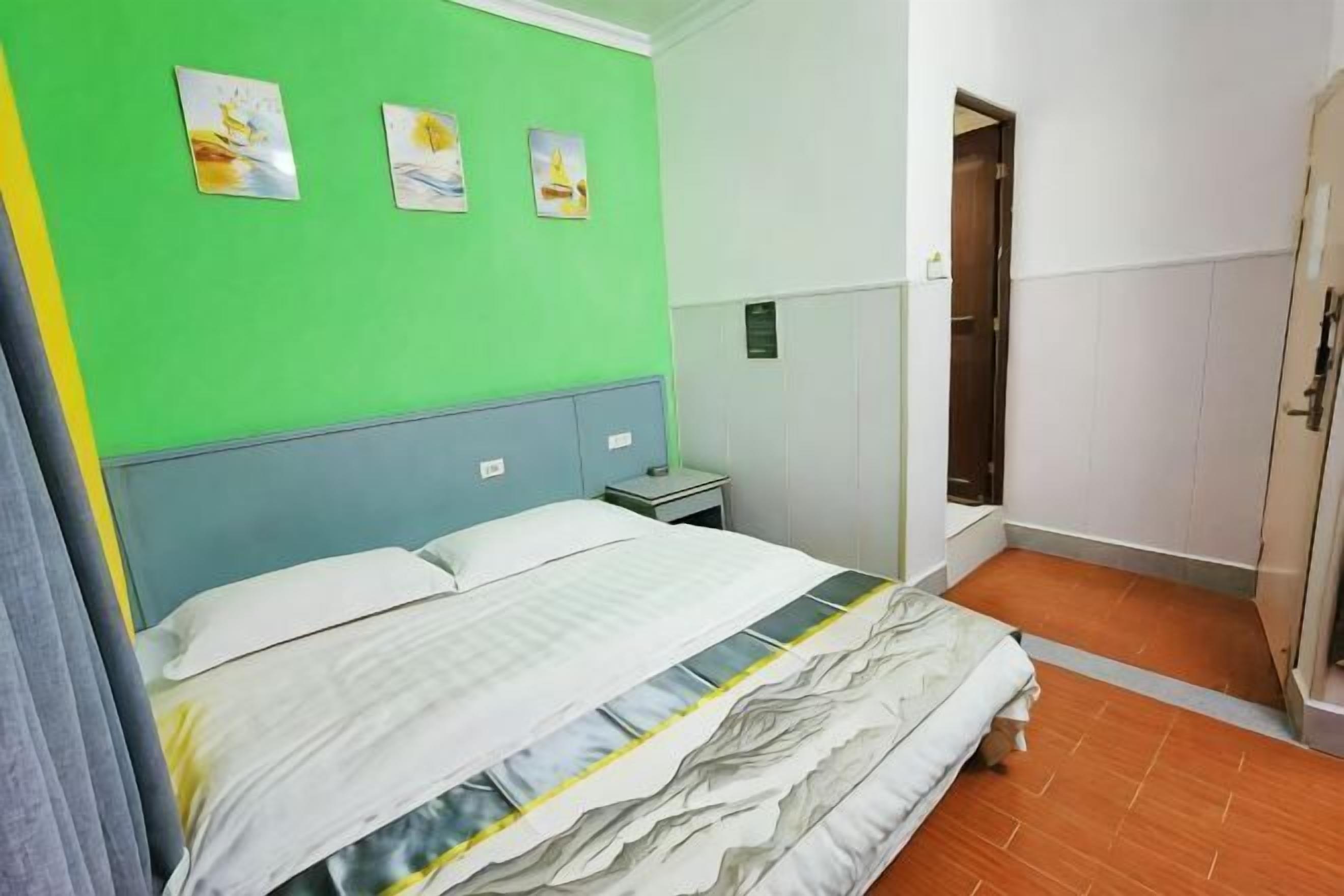 A bedroom with a bed, a nightstand, a green wall, and a bathroom with a shower.