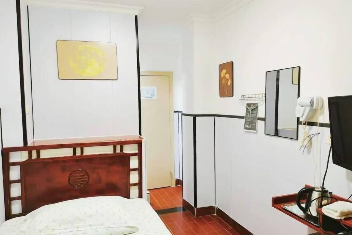A hotel room with a bed, a bedside table, a mirror, a wall-mounted TV, and a small red tray with a hairdryer.