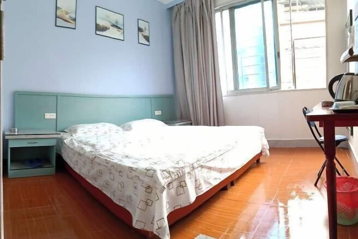 A bedroom with a bed, a nightstand, a desk, and a window with curtains.